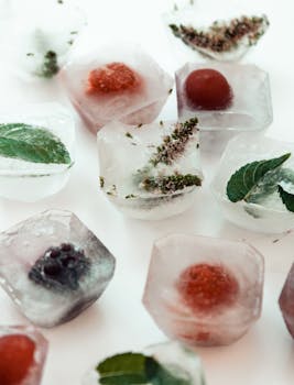 Close-up of ice cubes with berries and herbs on a white surface, perfect for summer themes.