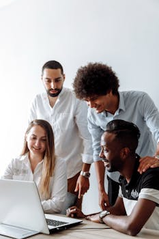 A diverse group of professionals happily collaborating on a laptop in an office setting.