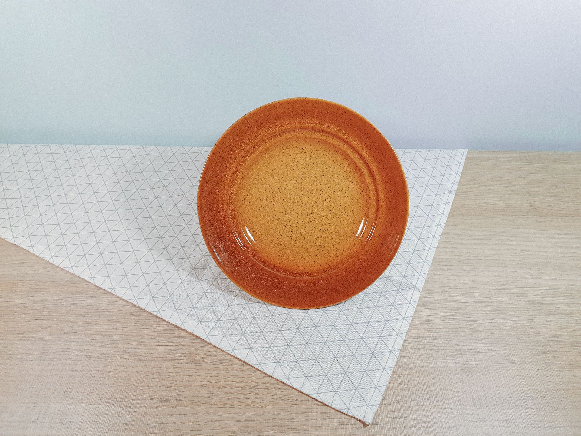Orange ceramic plate on a wooden table with geometric pattern, perfect for rustic kitchen decor.