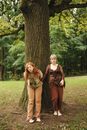 Woman in Black and Brown Dress Sitting on Ground Beside Brown Tree
