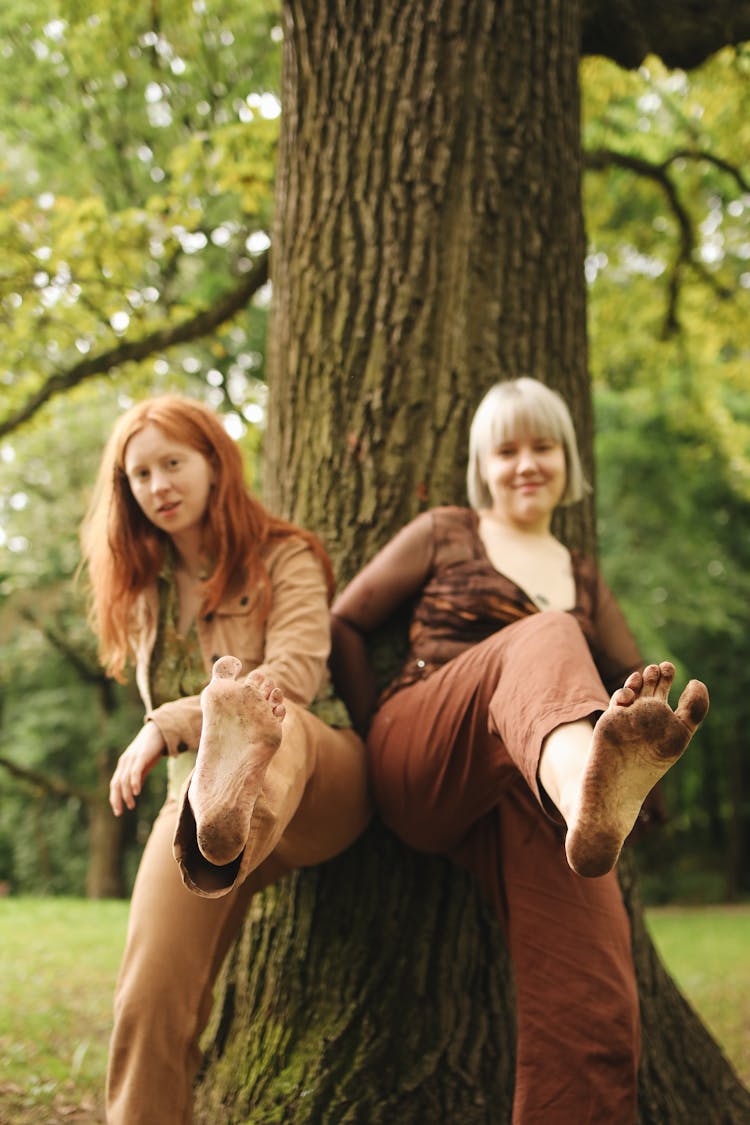 Women Leaning On The Tree While Showing Their Dirty Feet