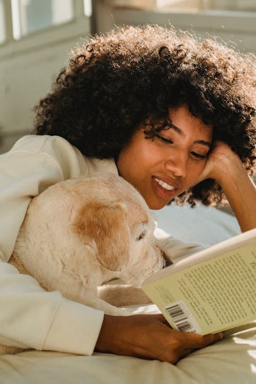 무료 휴식 하 고 침대에 강아지와 함께 읽는 쾌활 한 흑인 여성 스톡 사진