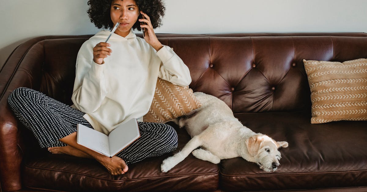 Thoughtful black woman with notebook and dog on leather sofa
