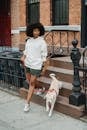 Full length of black female with Afro hairstyle holding leash while going for walk with obedient dog