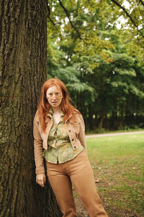 A Woman in Brown Jacket and Pants Leaning on the Tree