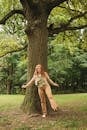Woman in White Shirt and Brown Pants Sitting on Tree Branch