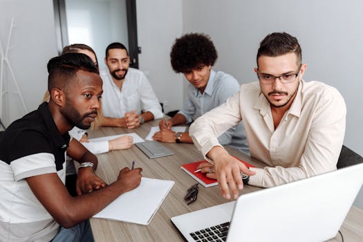 A diverse group of professionals engaged in teamwork at a modern office setting with laptops and notebooks.
