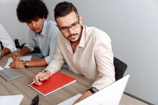 Two professionals brainstorming at an office, focused on teamwork and planning with a laptop.