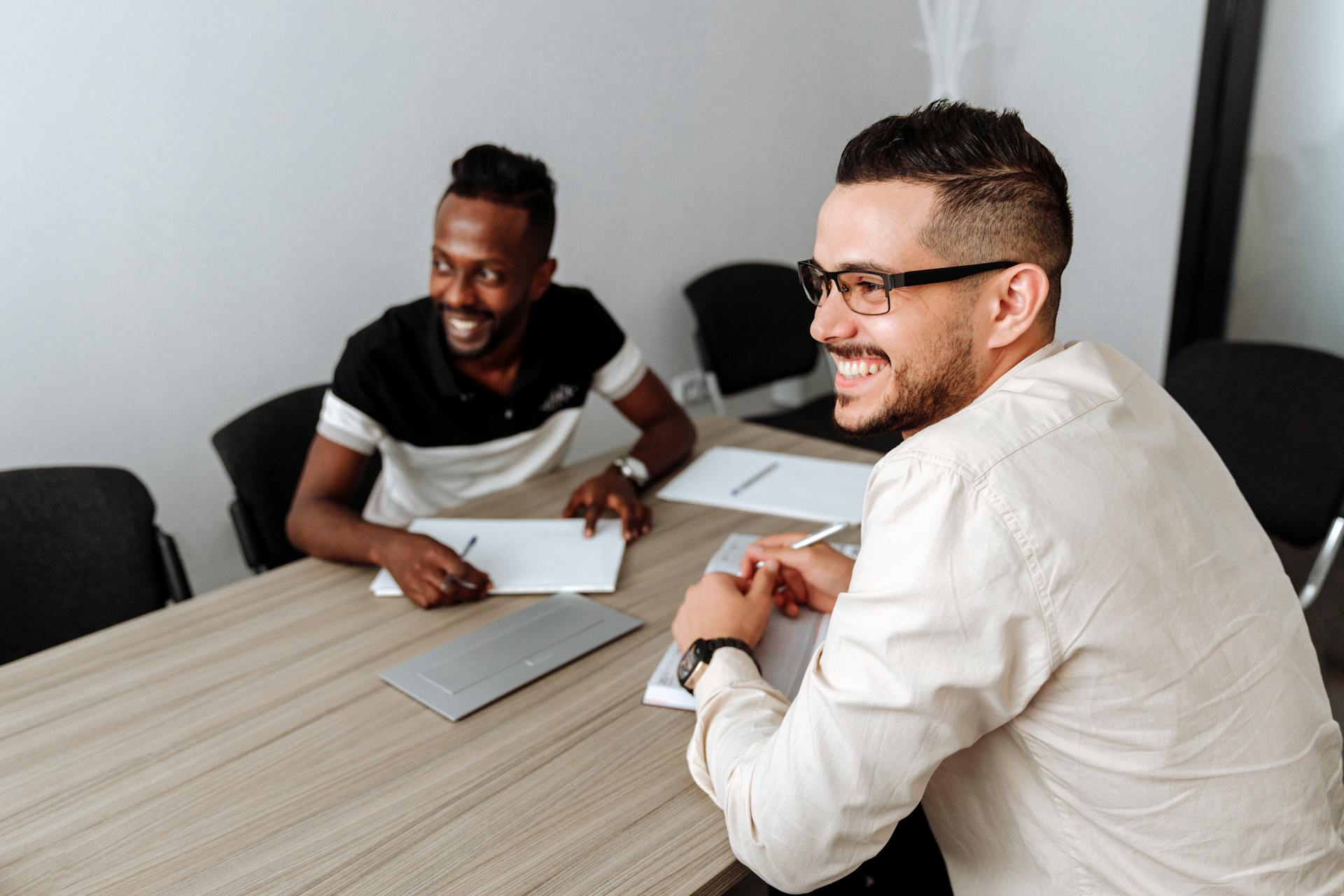 Two businessmen smiling during a meeting in a modern office setting.