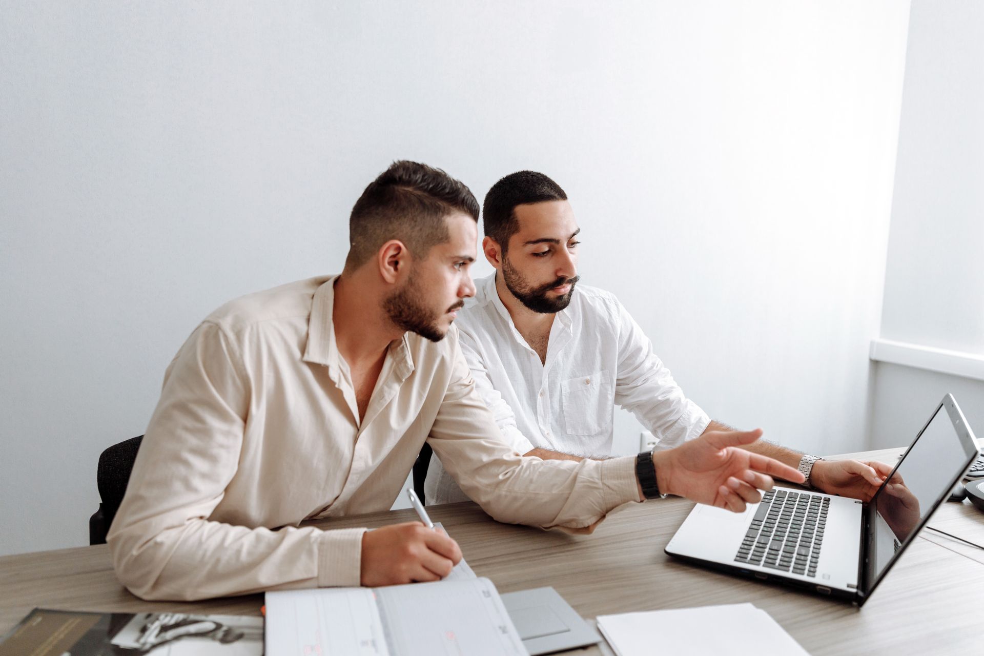 Two men working together on a laptop during a business meeting indoors.