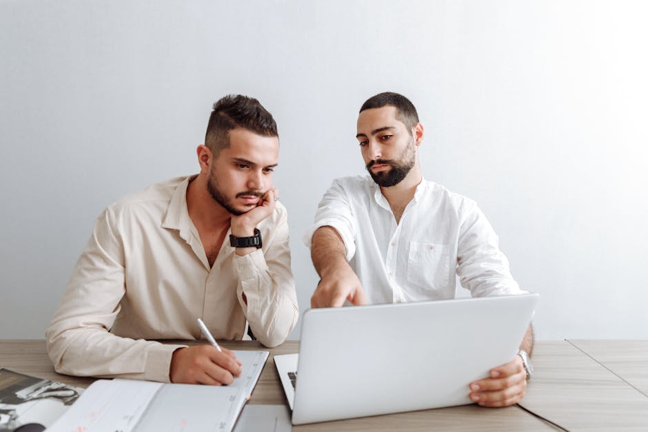 Two businessmen working together on a laptop in an office setting, focusing on a project. Two businessmen working together on a laptop in an office setting, focusing on a project.