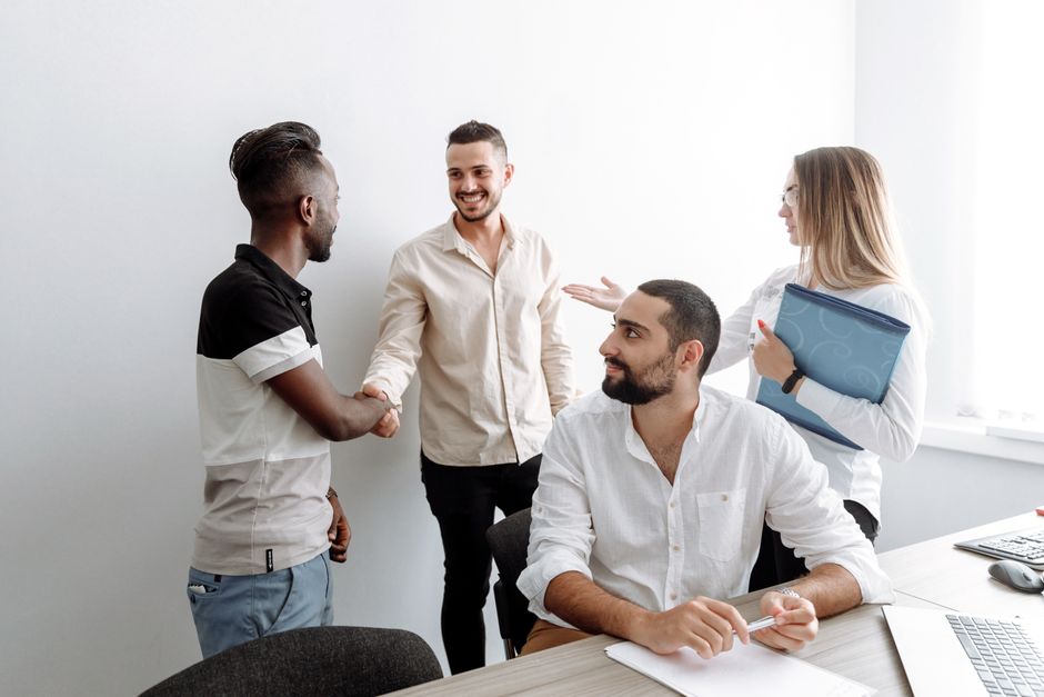 Uma equipe de profissionais diversos apertando as mãos e sorrindo em um ambiente de escritório, simbolizando cooperação.