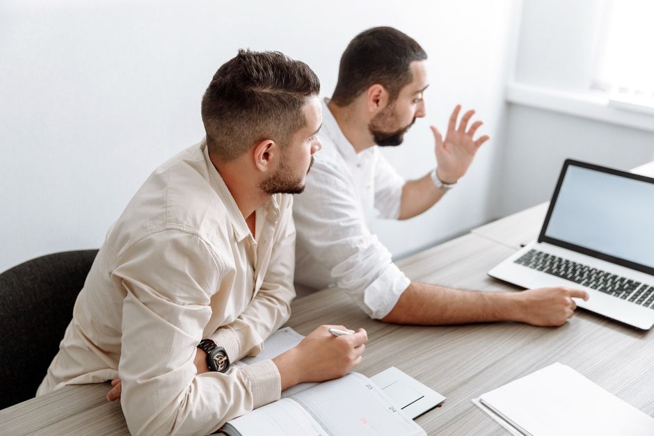 Two adult men collaborating in a modern office setting, discussing ideas with a laptop. Two adult men collaborating in a modern office setting, discussing ideas with a laptop.