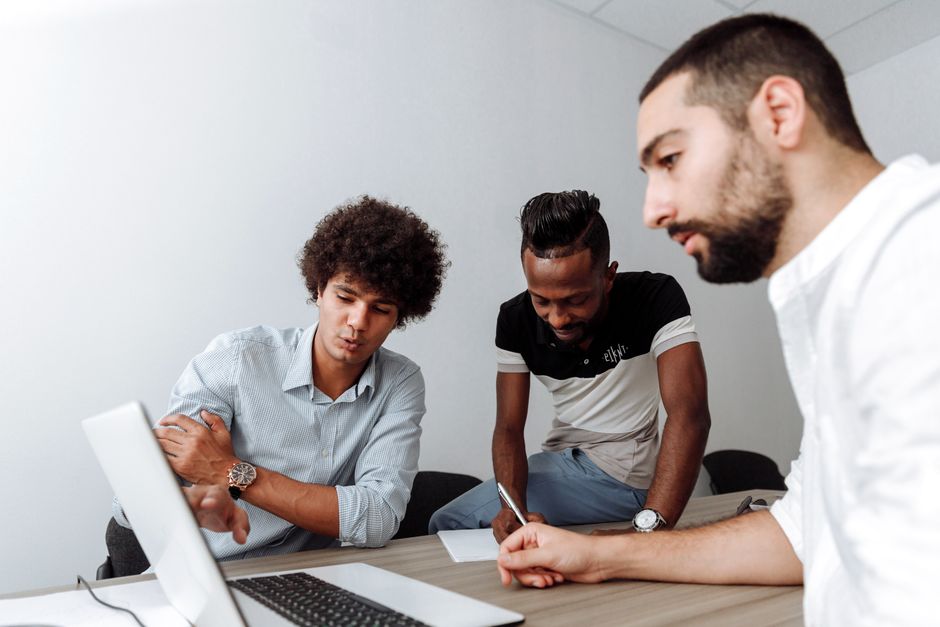 Diverse group of young men collaborating in an office meeting room with a laptop. Diverse group of young men collaborating in an office meeting room with a laptop.