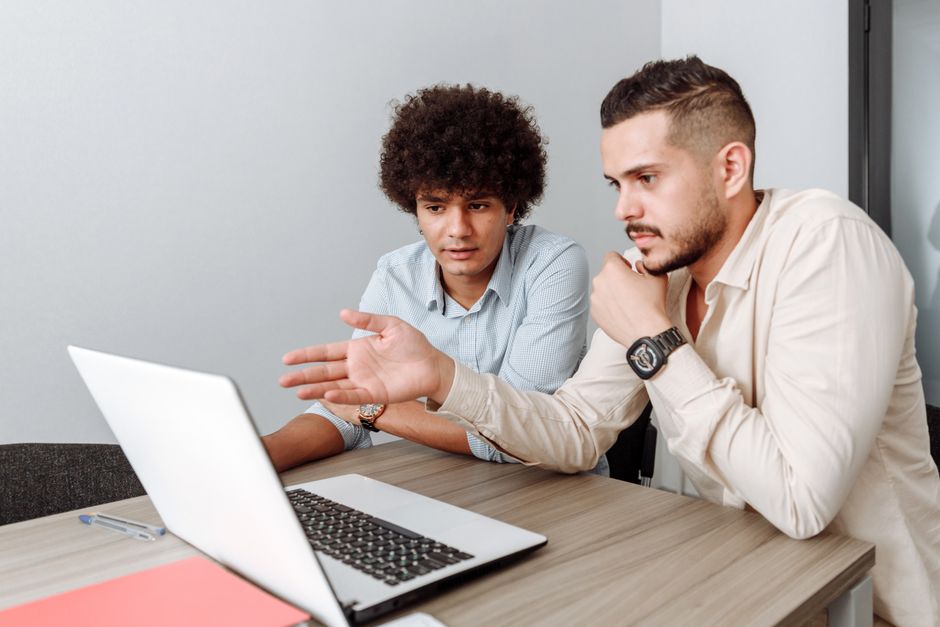 Two young men working together on a laptop in a modern office setting. Two young men working together on a laptop in a modern office setting.