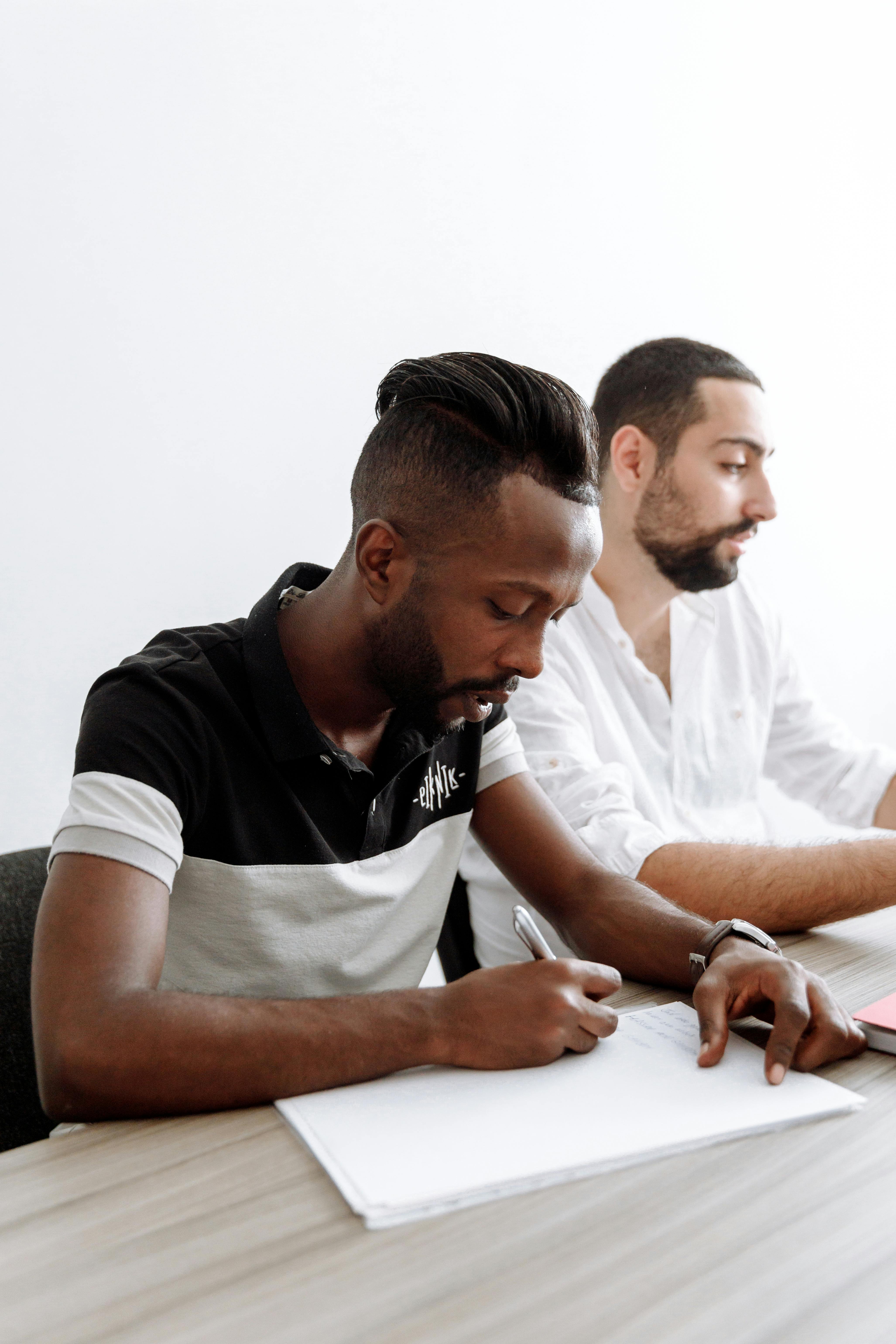 两名男子在明亮的办公室里合作，一边做着笔记