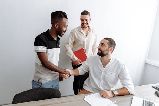 Three men in an office setting engaging in a friendly handshake, showcasing teamwork and collaboration.