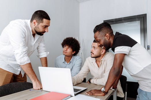 Diverse group of business professionals engaging in a collaborative meeting around a laptop.