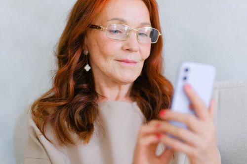 Free Elegant middle-aged woman with glasses using a smartphone indoors. Stock Photo