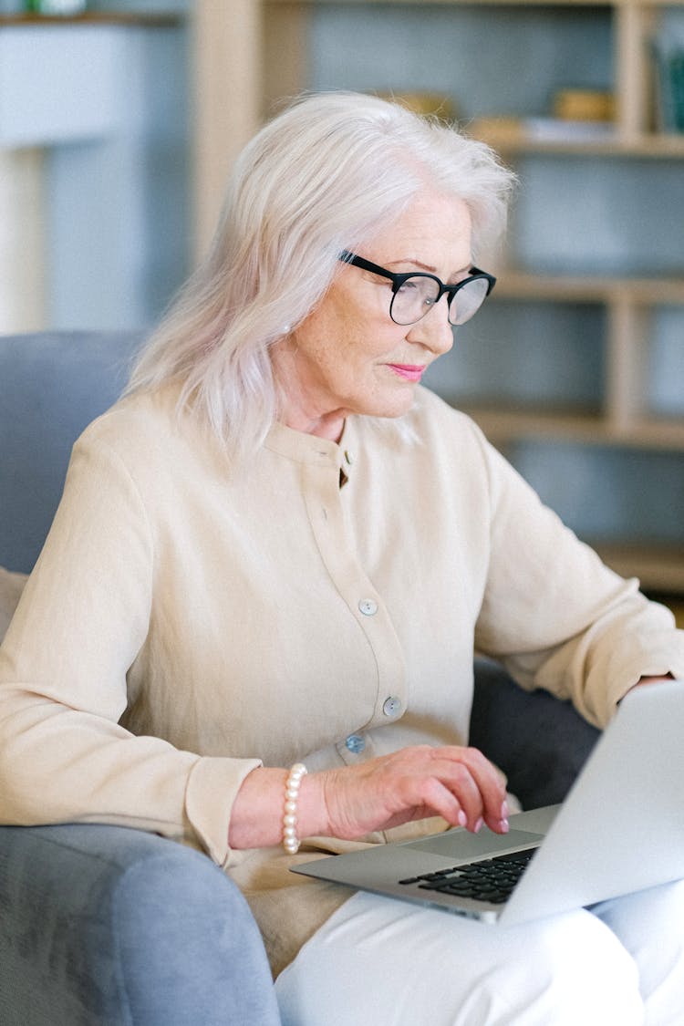 Aged Woman In Eyeglasses Surfing Internet On Laptop