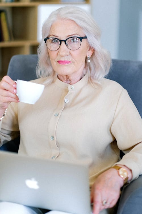 Aged woman with cup of coffee with modern convenient laptop