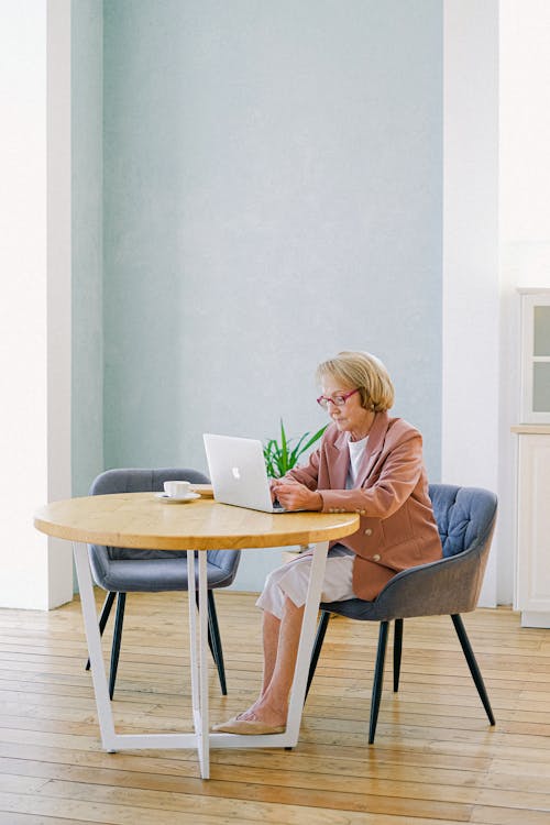 Free Woman in Blue Long Sleeve Shirt Sitting on Chair Using Macbook Stock Photo