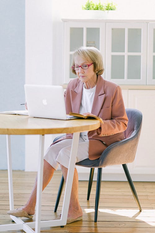Senior experienced woman in eyeglasses working with laptop