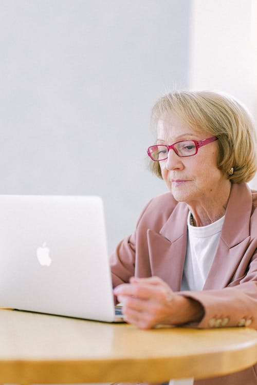 Focused elderly female in eyeglasses working on new business project while using netbook at table