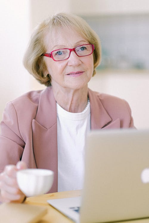 Senior woman with cup working on remote job on laptop