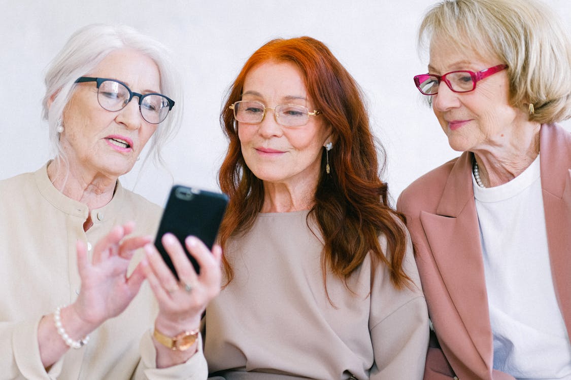 Free Happy aged women in eyeglasses looking at screen of smartphone Stock Photo