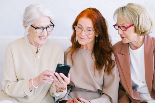 Free Group of cheerful elderly women in eyeglasses looking at screen of mobile phone together Stock Photo