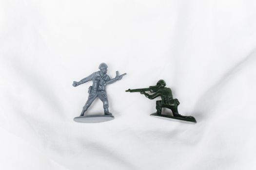 Two toy soldier figurines on a white background. One stands and one is prone, depicting a playful battle scene.