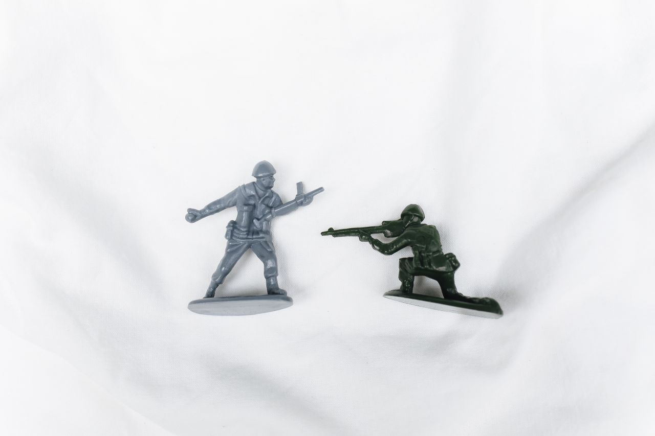 two toy soldier figurines on a white background one stands and one is