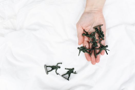 A hand gently holding army toy soldiers on a white fabric, perfect for conceptual or thematic projects.