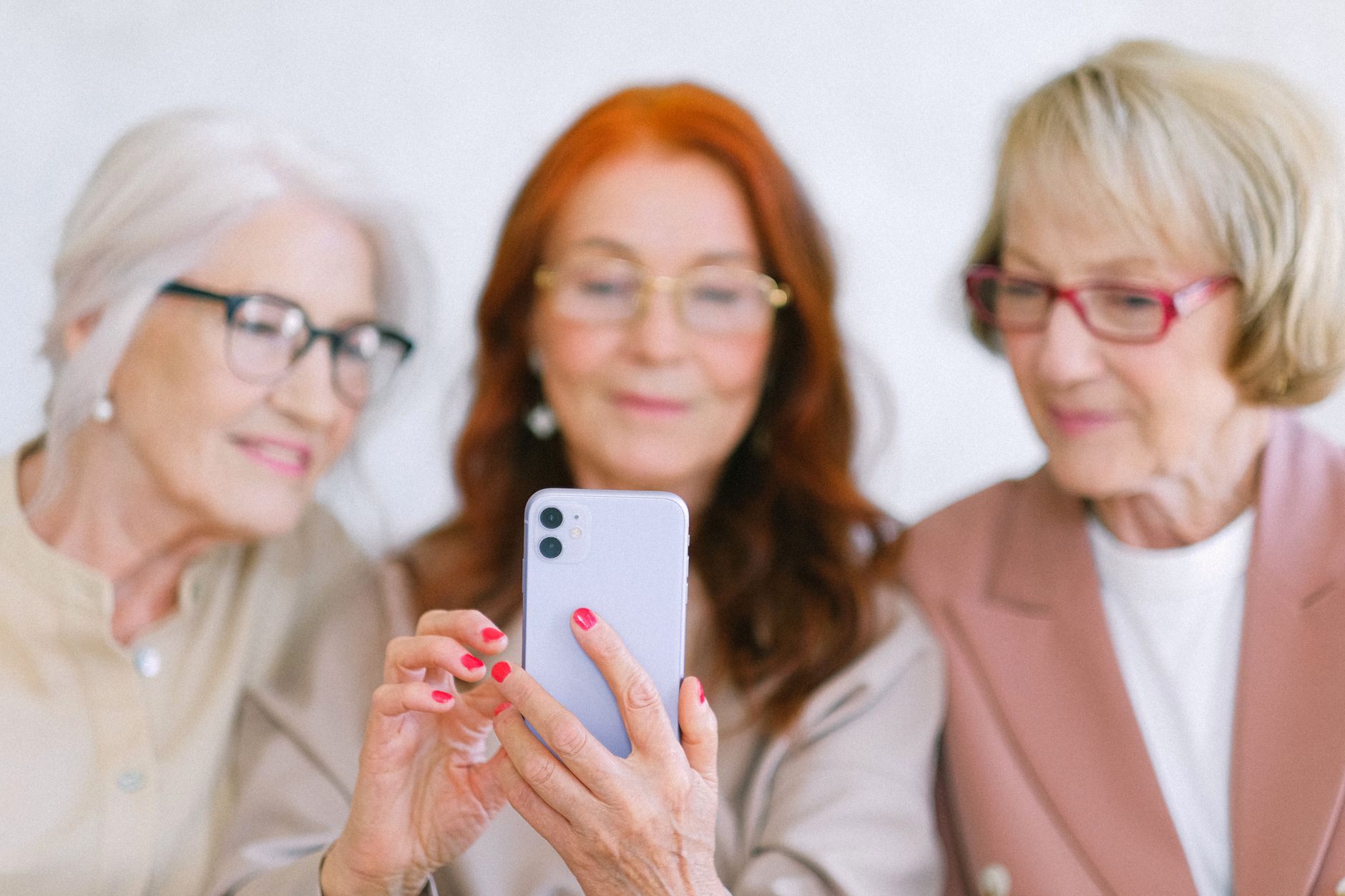 경기도 어르신 스마트폰 무료 교육 3 Three senior women using a smartphone indoors, sharing a joyful moment together.