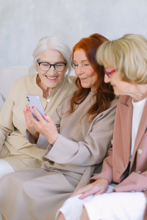 Free Senior cheerful women in eyeglasses looking at screen of smartphone and surfing internet together Stock Photo