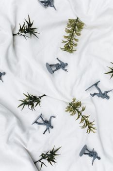 Flat lay of toy soldiers and leaves on white fabric background.