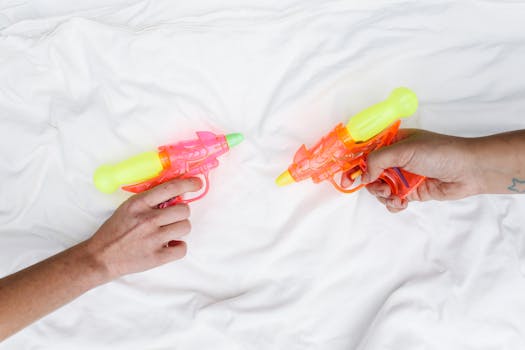 Hands holding colorful toy water guns, involved in a playful duel on a white background.