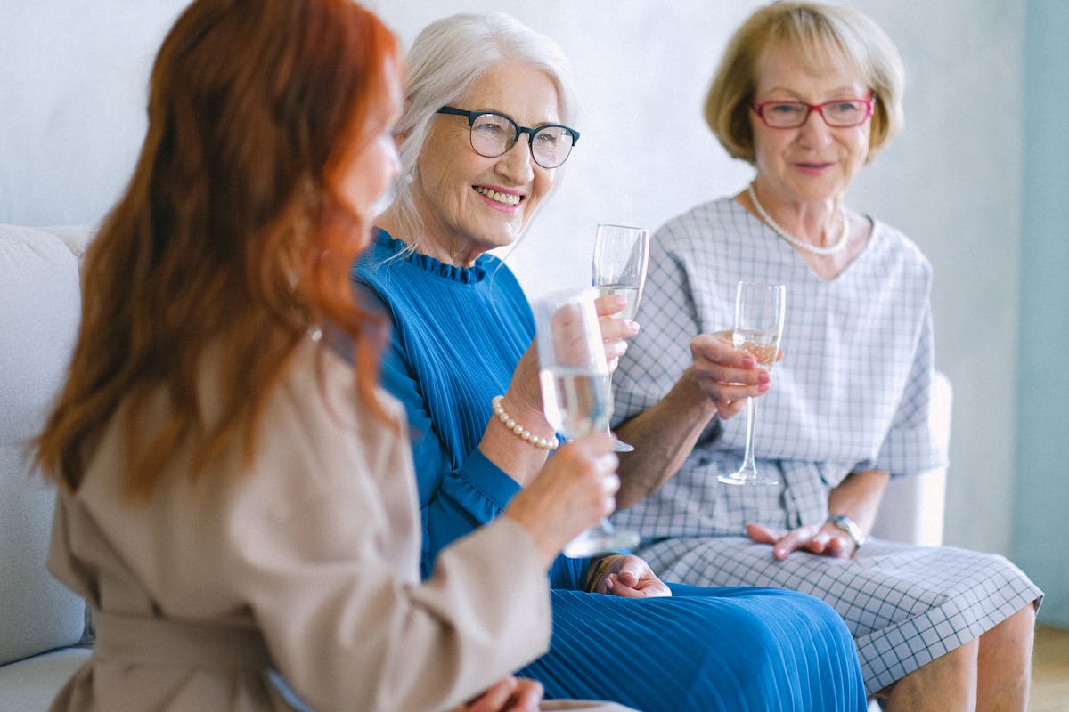 Elderly cheerful women with glasses of champagne smiling and chatting while celebrating special festive event