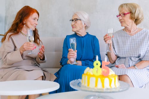 Free Aged best friends with glasses of champagne talking at table with birthday cake decorated with candles Stock Photo