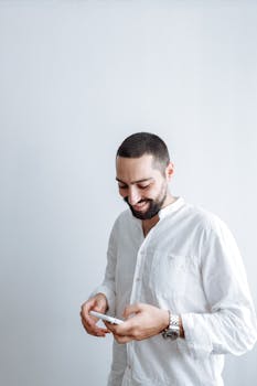 一个开朗的男人穿着白衬衫，在室内检查他的智能手机