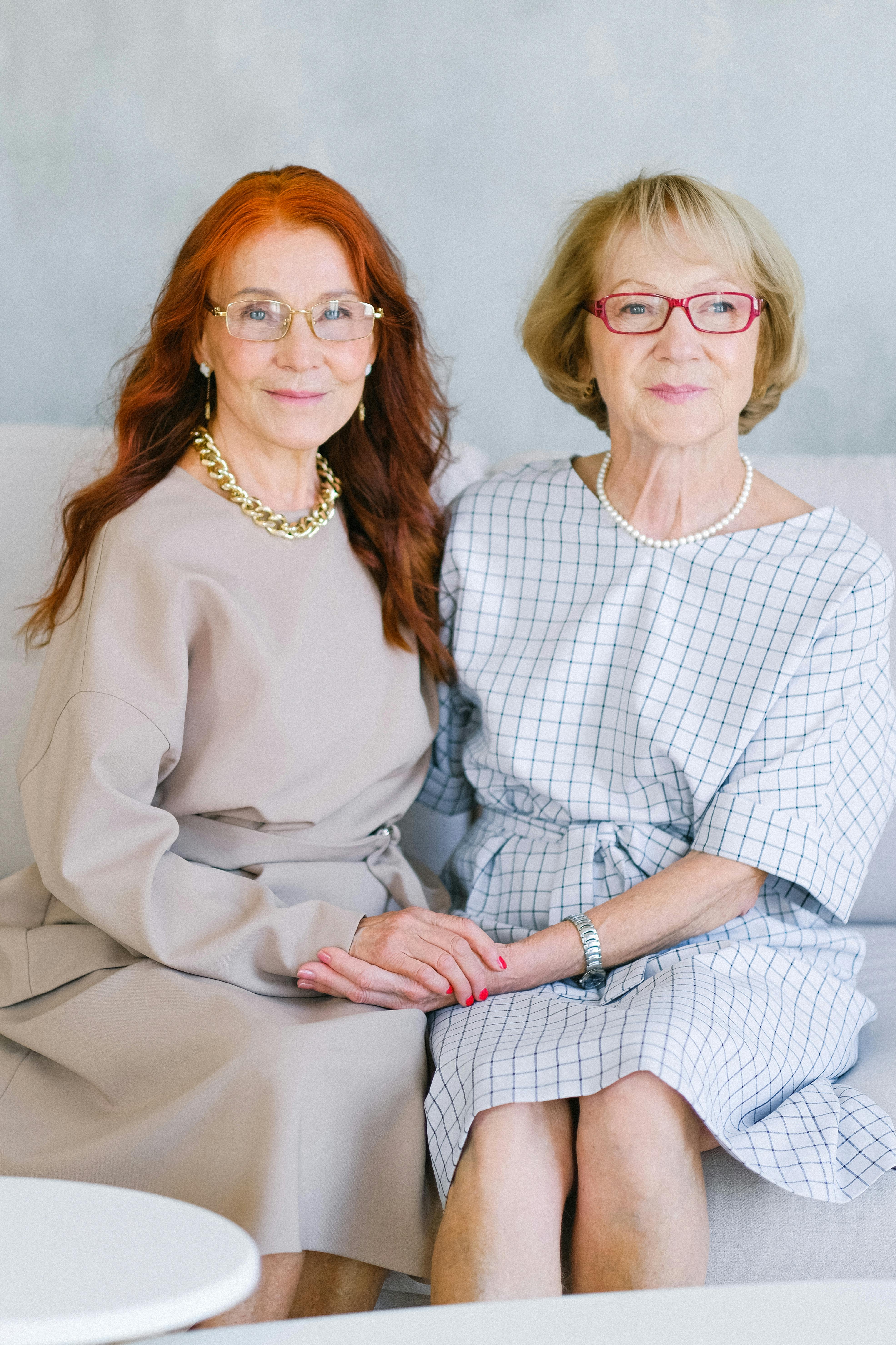 Happy pleasant elderly women in eyeglasses touching hands and looking at camera while smiling