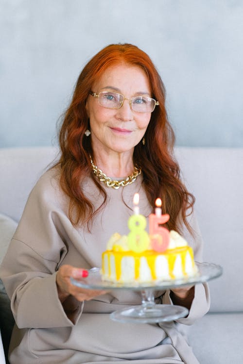 Happy aged woman with birthday cake decorated with festive candles