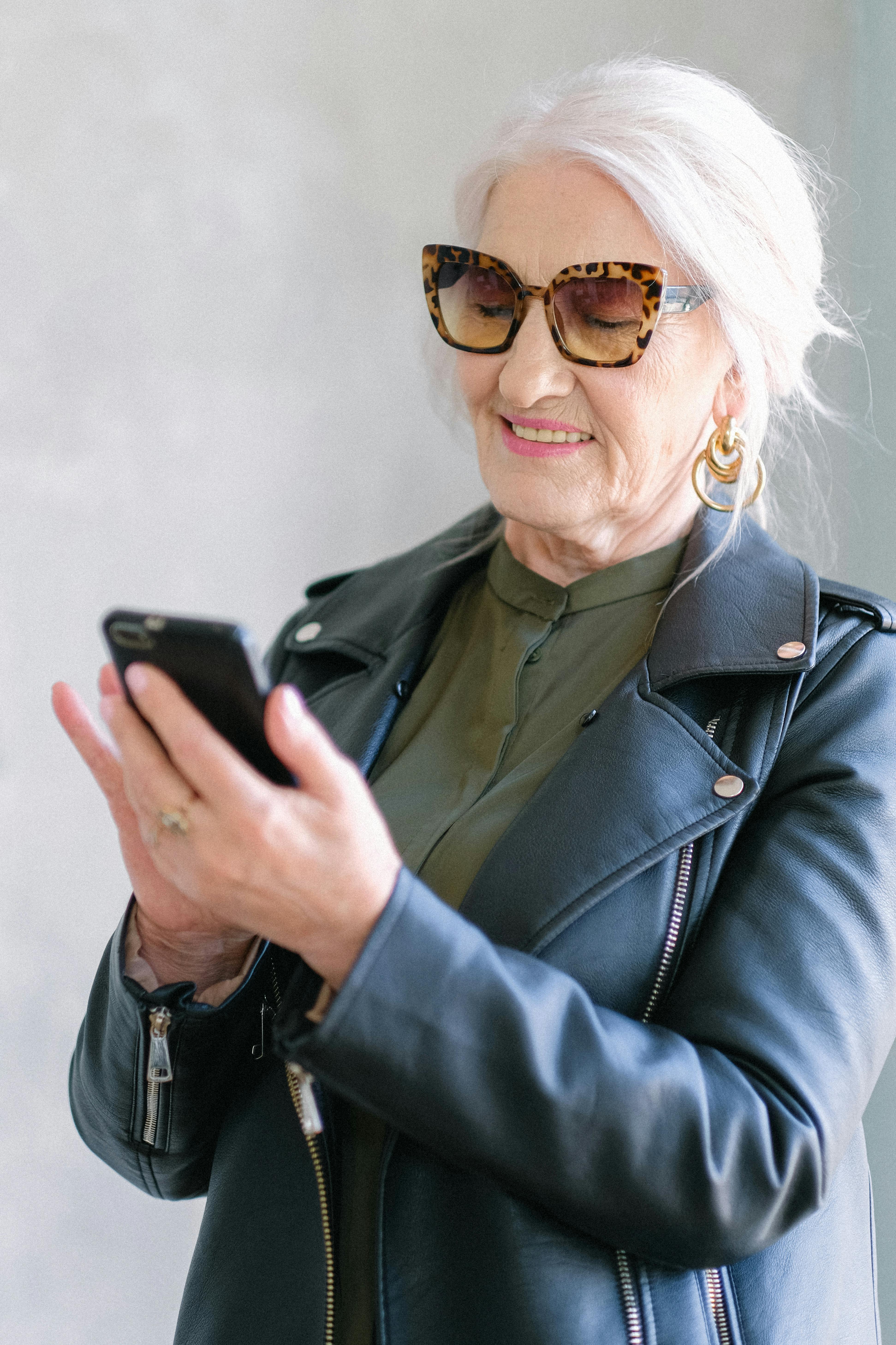 stylish elderly woman in trendy jacket checking smartphone
