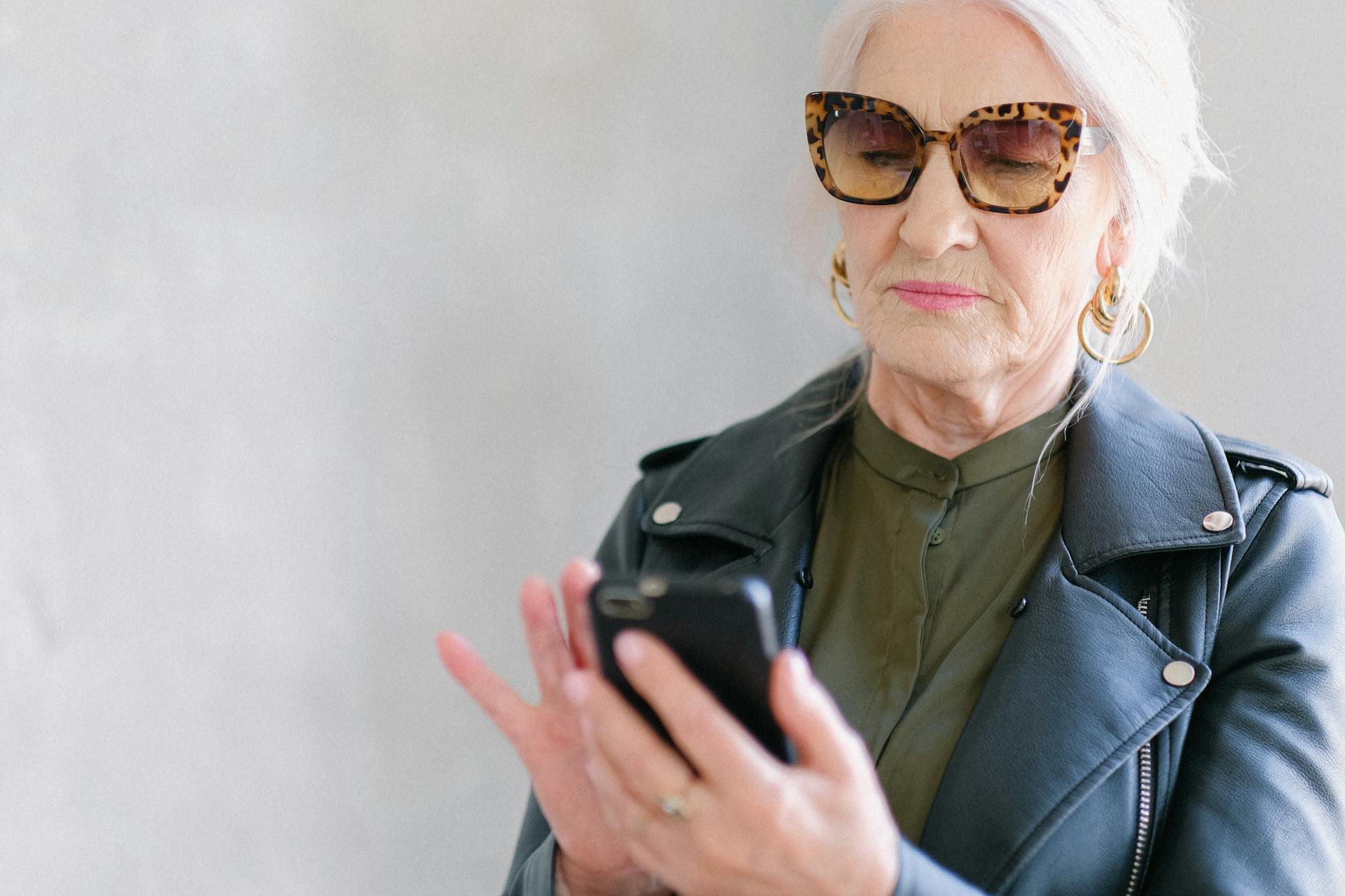 Aged woman in trendy sunglasses touching screen of smartphone