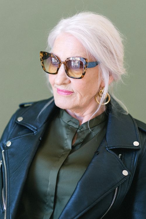 Free Elderly female in stylish sunglasses and jacket looking away on green background of studio Stock Photo