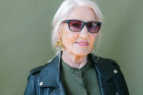 Free Crop aged confident female in stylish leather jacket and sunglasses looking at camera on green background of studio Stock Photo