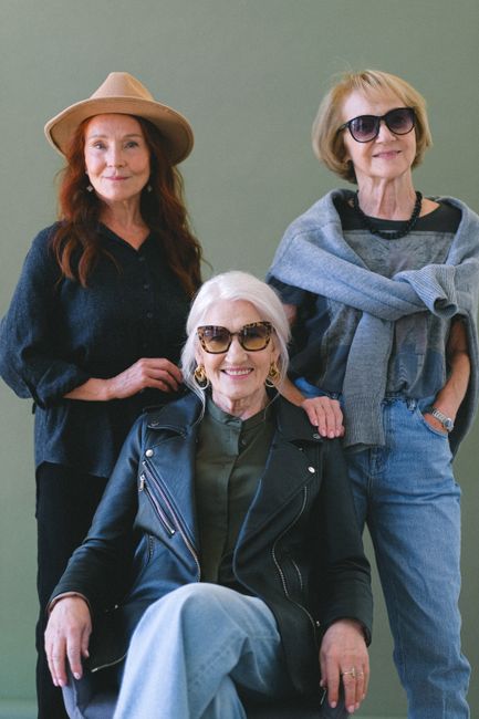 Group of cheerful aged women in stylish outfit smiling and looking at camera on green background