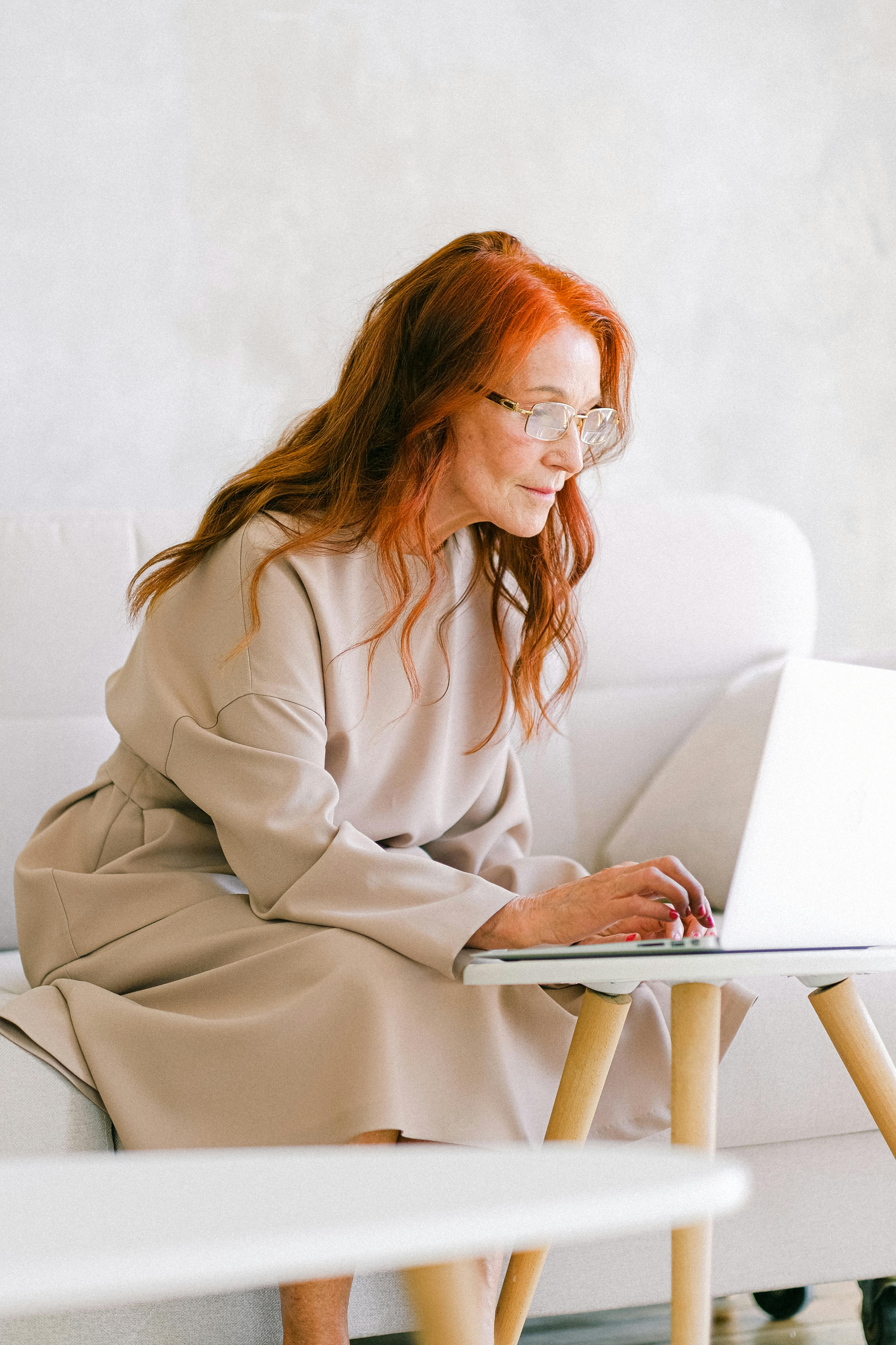 elderly woman with red hair typing on keyboard of laptop