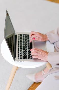 From above of crop anonymous elderly female typing on keyboard of netbook while surfing internet